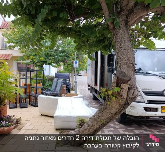 משאית הובלה עם רהיטים על המדרכה ליד עץ